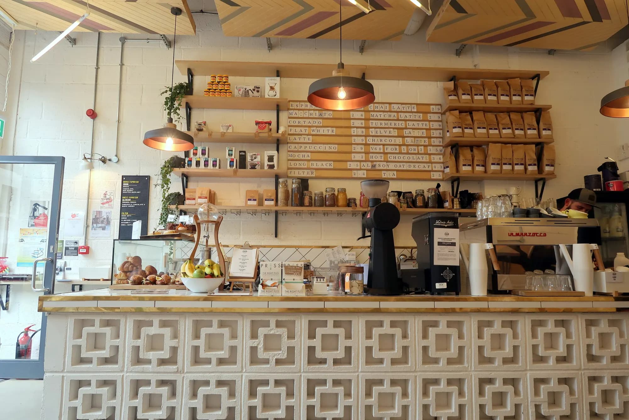 The counter of a London coffee bar, with an espresso machine, grinder, shelves of coffee bags and pastries.