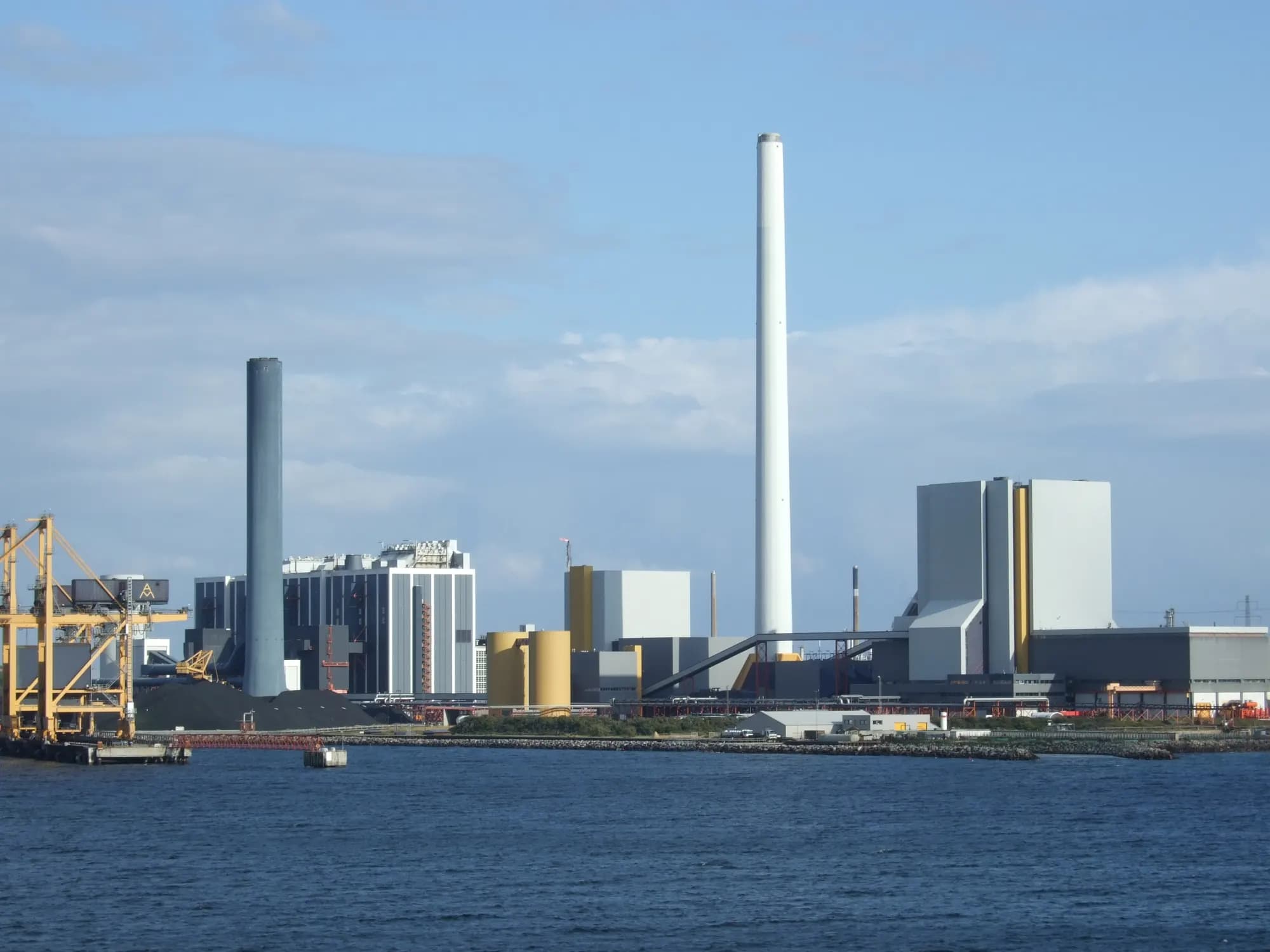 A power station with a tall white chimney and coal cranes on the waterfront at Kalundborg, seen across the water.