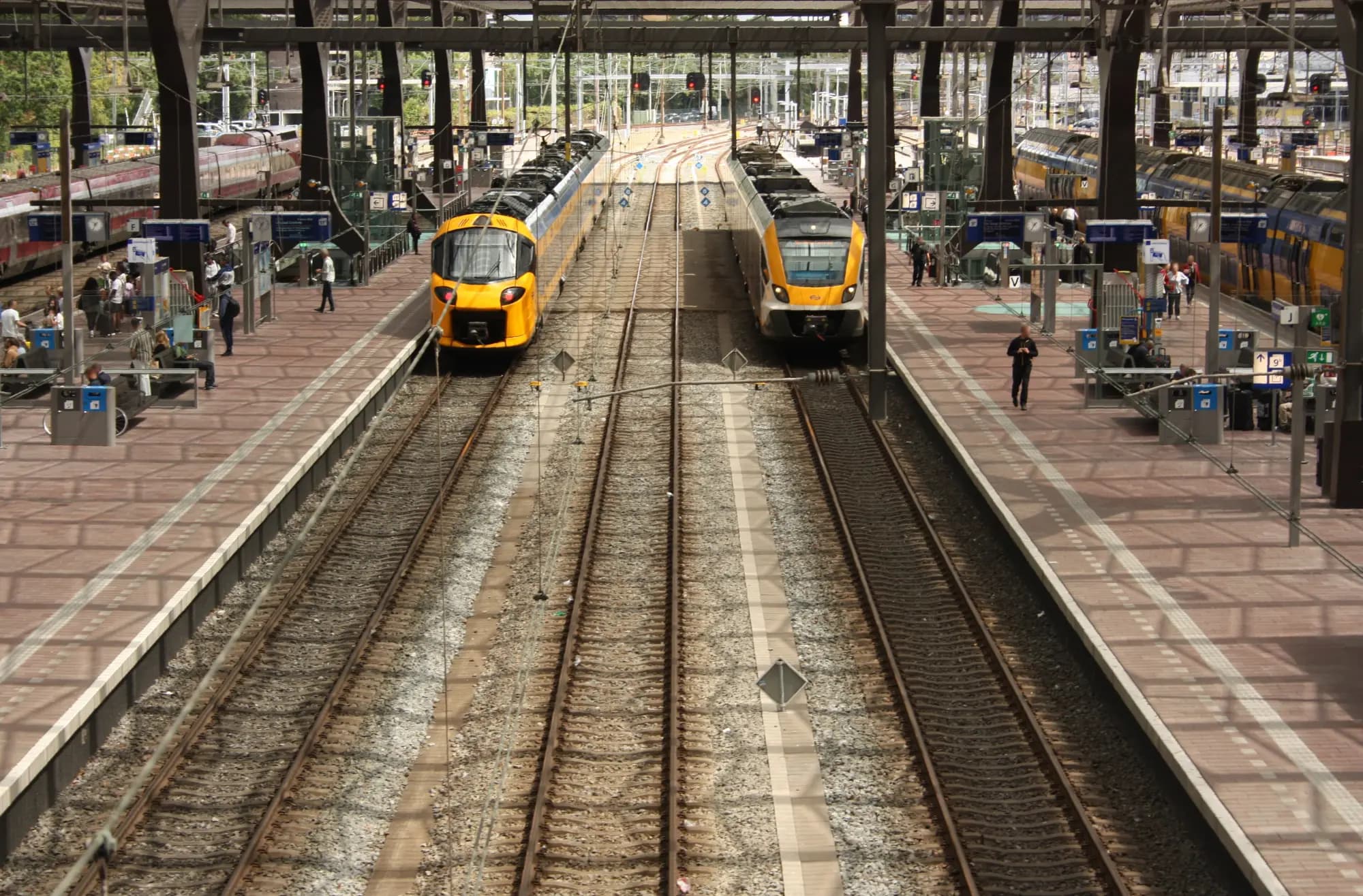 Platforms of Rotterdam Centraal seen from a footbridge, with two yellow NS trains standing at the platforms.