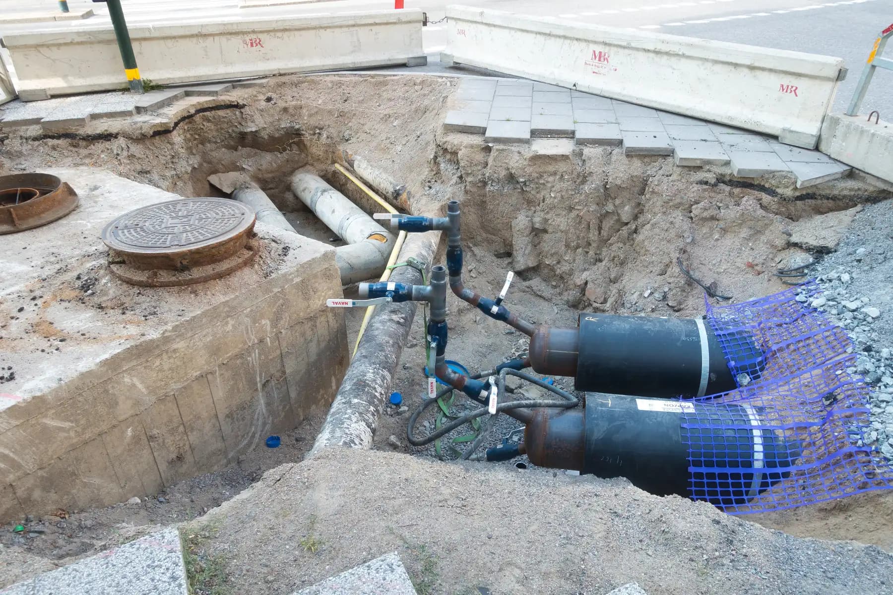 An open trench in a Stockholm street with insulated district heating pipes and valves being connected.